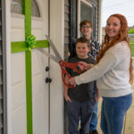 three people standing in front of a door with ribbon and scissors